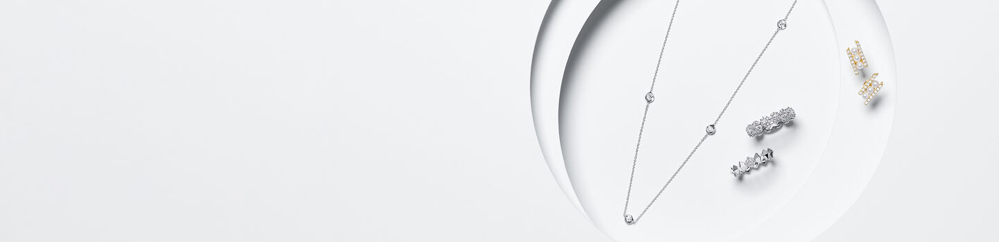 pearl necklace next to 2 white gold rings and a pair of yellow gold earrings.